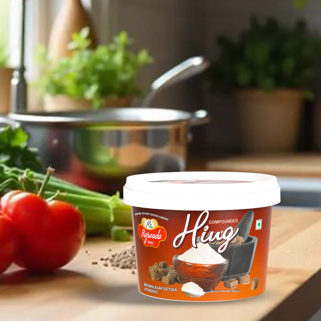 Container of compounded hing- Rajwada Hing on a kitchen counter with vegetables in the background