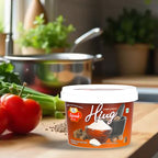 Container of compounded hing- Rajwada Hing on a kitchen counter with vegetables in the background