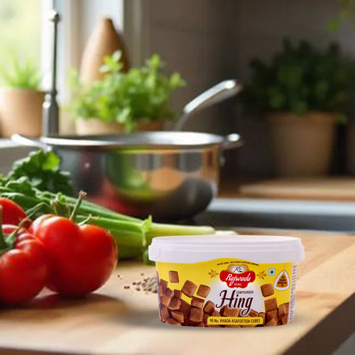 Container of Premium Hing Cubes – Strong Aroma & Authentic Indian Flavor on a kitchen counter with vegetables and cooking utensils in the background